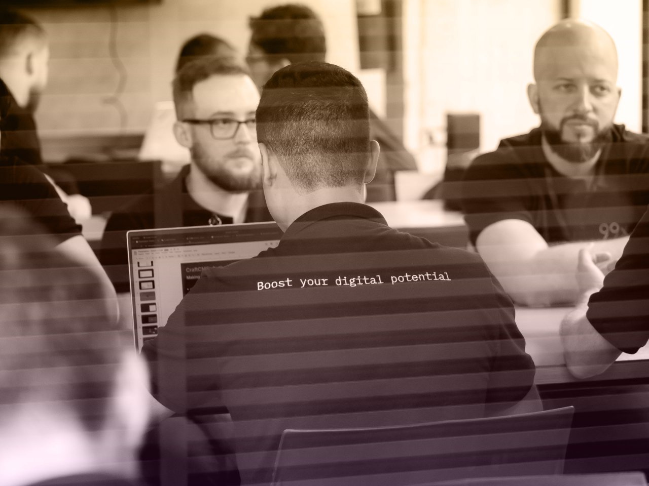 Group of people in black t-shirts with 'Boost your digital potential' printed on the back, collaborating in an office setting.