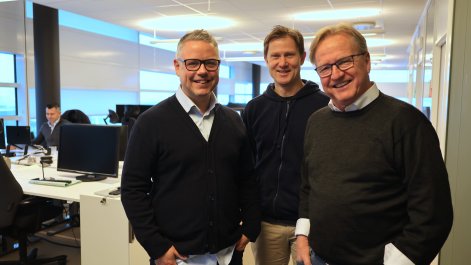 Tre menn poserer foran kamera på kontoret