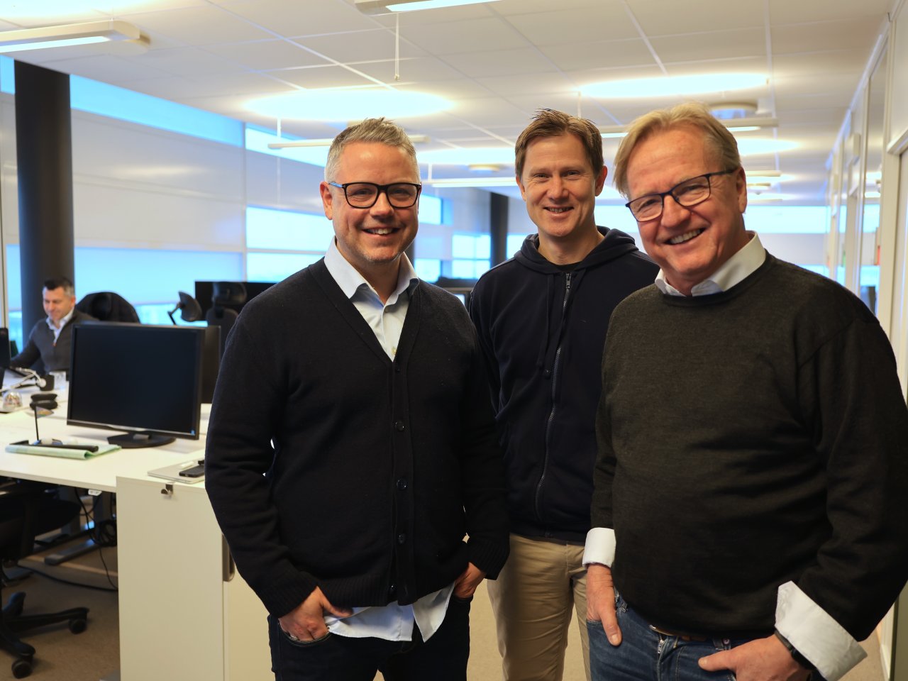 Tre menn poserer foran kamera på kontoret