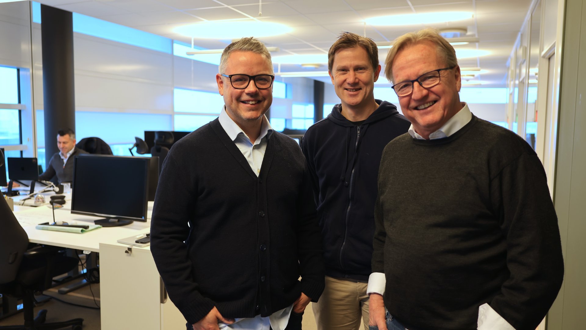 Tre menn poserer foran kamera på kontoret