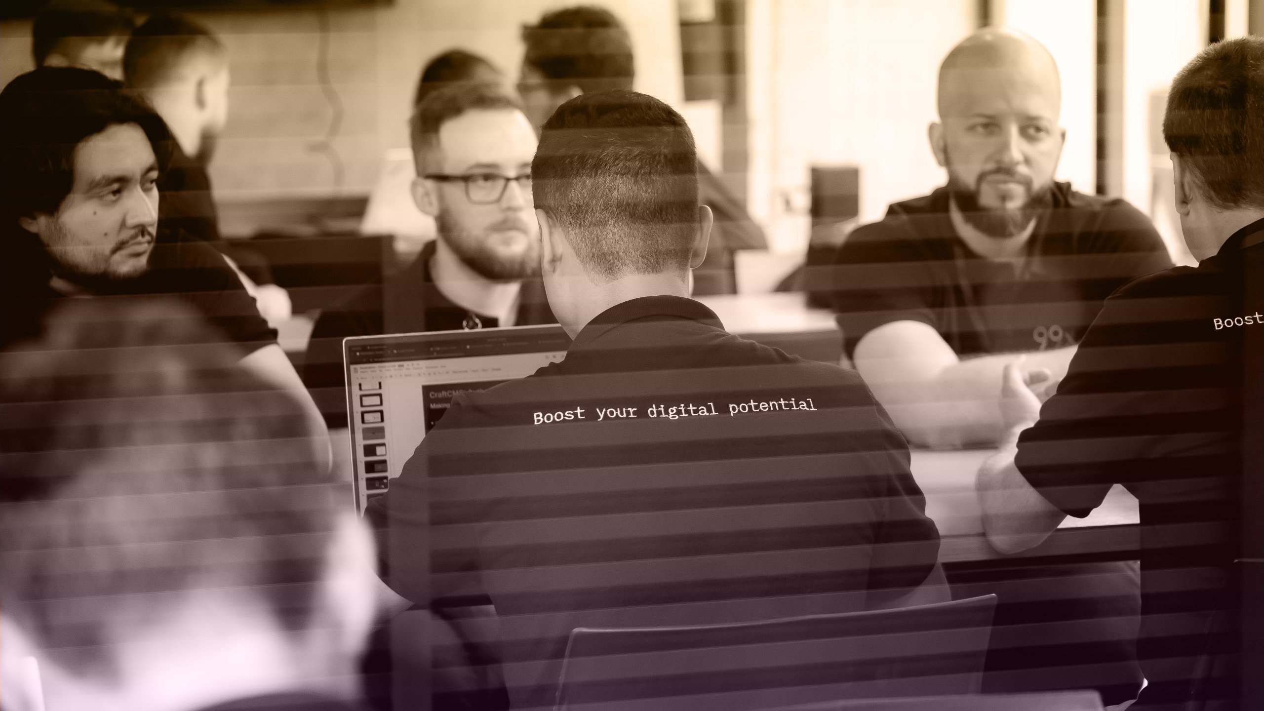 Group of people in black t-shirts with 'Boost your digital potential' printed on the back, collaborating in an office setting.